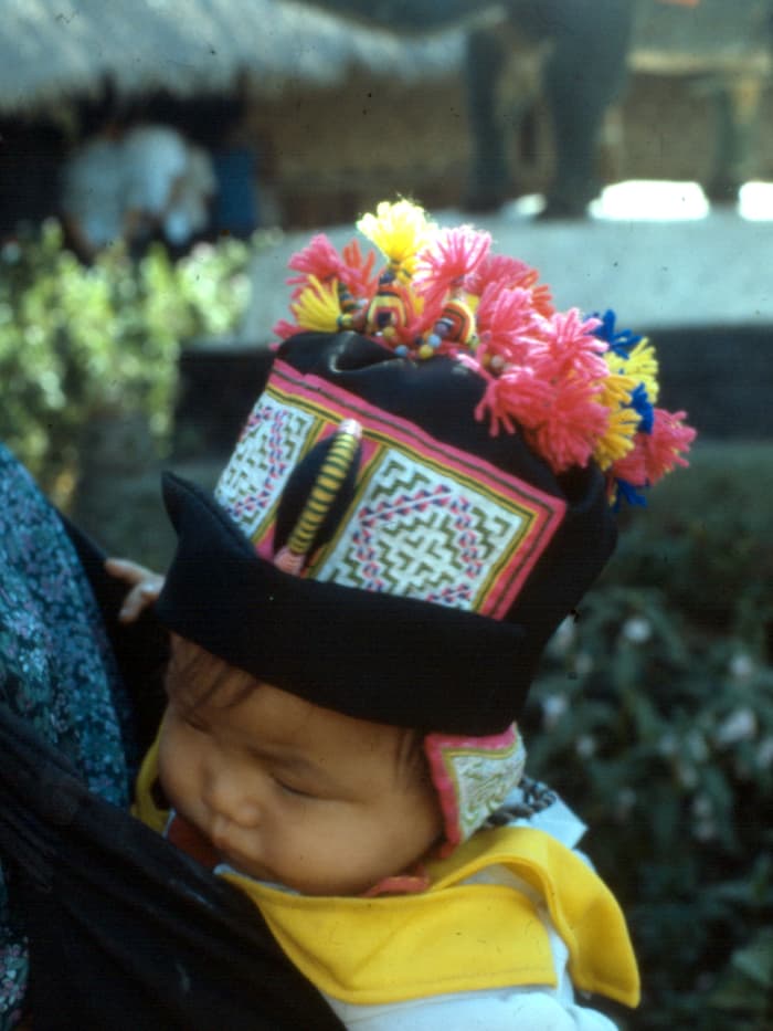 A child carried in an embroidered paj ntaub baby carrier