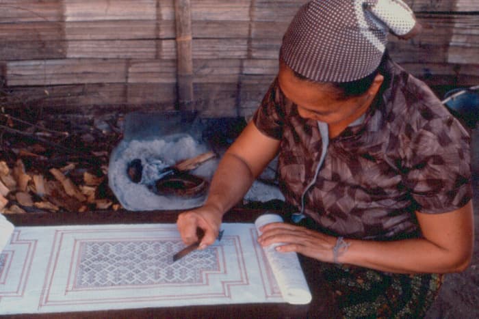A woman stitching a paj ntaub story cloth by hand